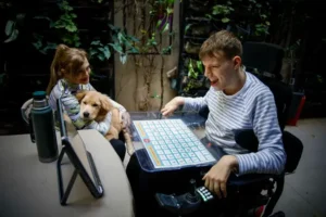 Iván Davidovich utilizando un tablero de Comunicación Aumentativa y Alternativa junto a su mamá y un perro, en una escena de apoyo y autonomía.